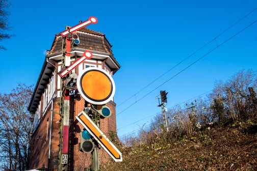 Ein historisches Stellwerk mit Signalanlage vor blauem Himmel. Das Gebäude ist aus Backstein und Fachwerk, umgeben von kahlen Bäumen.