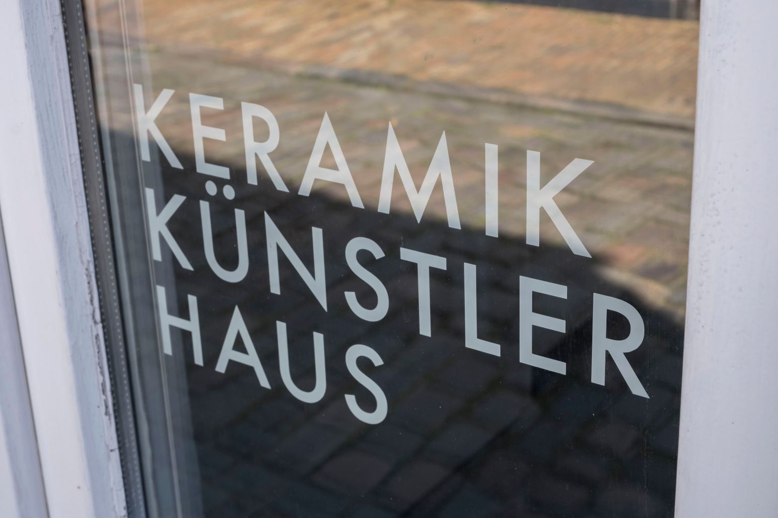Ein Glasfenster mit der Aufschrift 'Keramik Künstler Haus', das den Eingang zu einem Künstlerhaus zeigt.