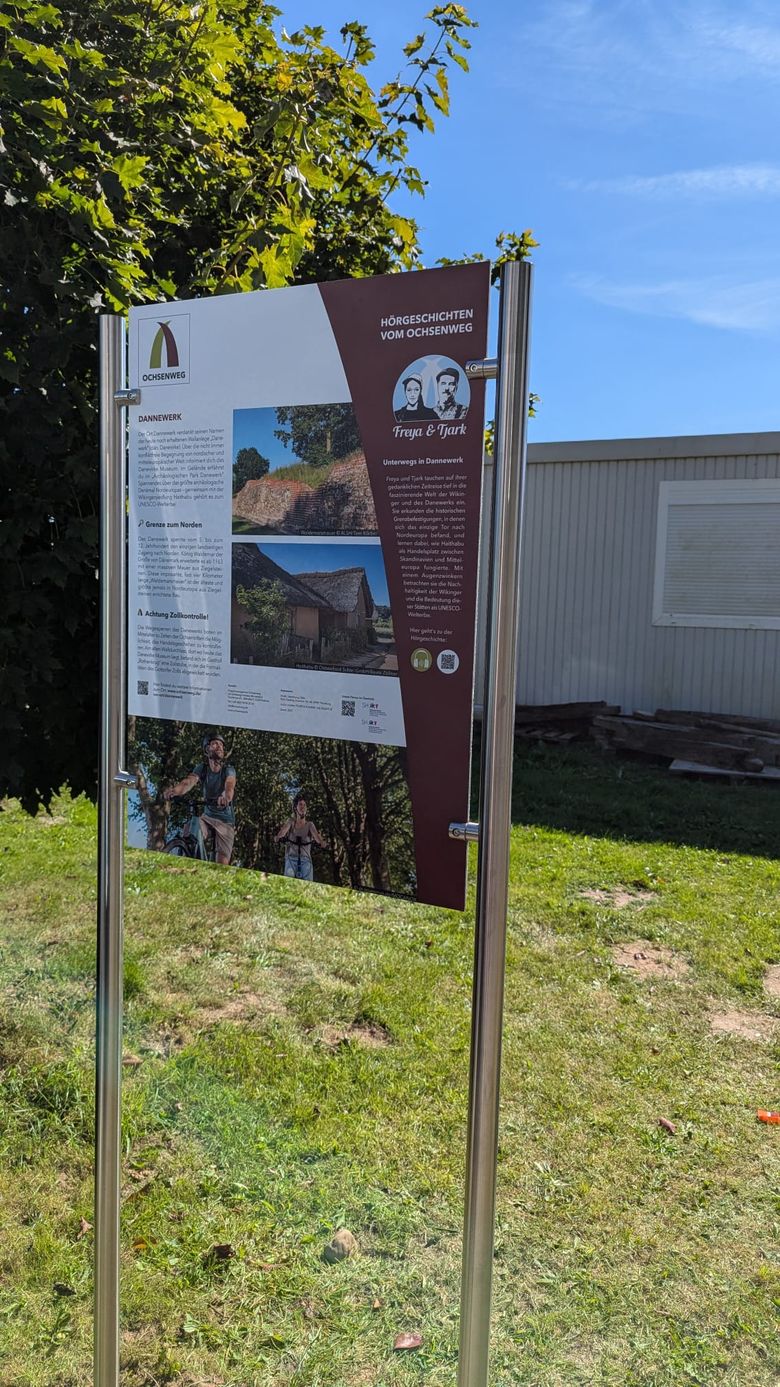 Ein Infotafel steht auf einer Wiese. Es enthält Texte und Bilder zur Geschichte und Bedeutung des Ortes.